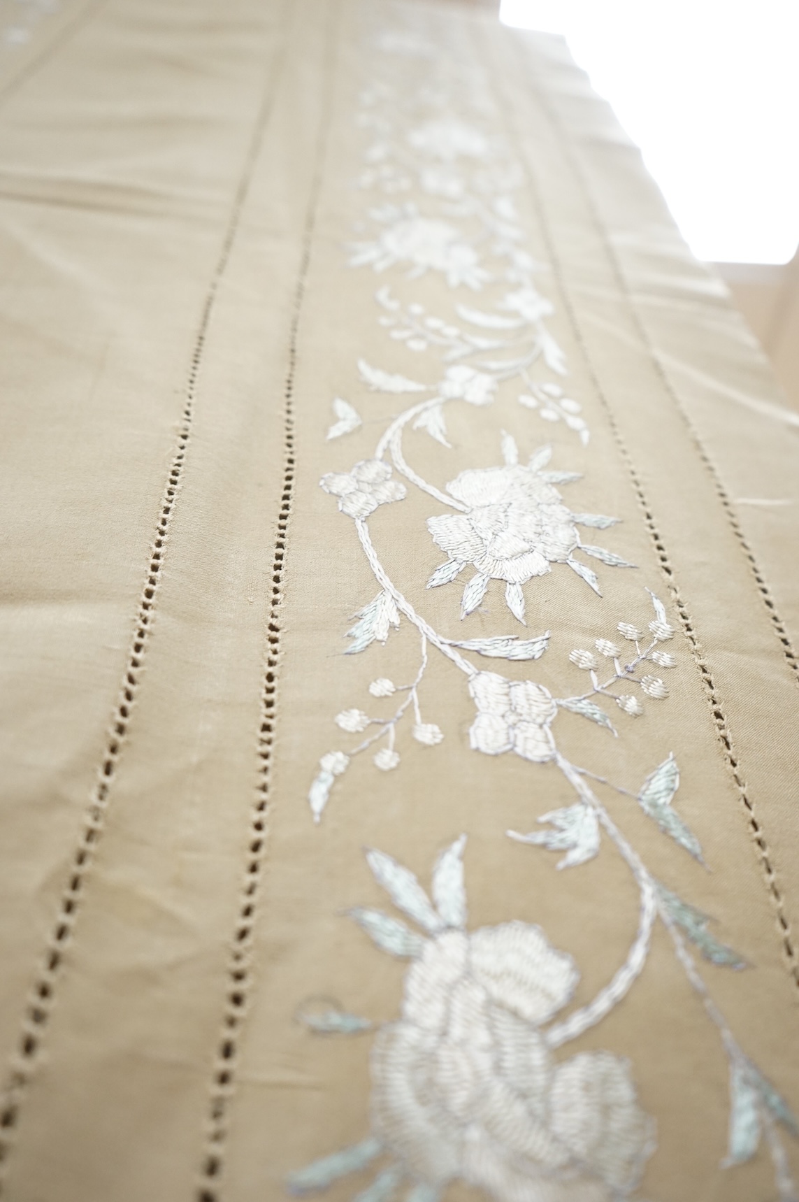 A 1920’s heavy shantung silk hand embroidered table cover. Worked with decorative rows of button hole stitch. Embroidered with white, green and blue silk flowers. 240cm x 204cm. Condition - some fine holes near corners,